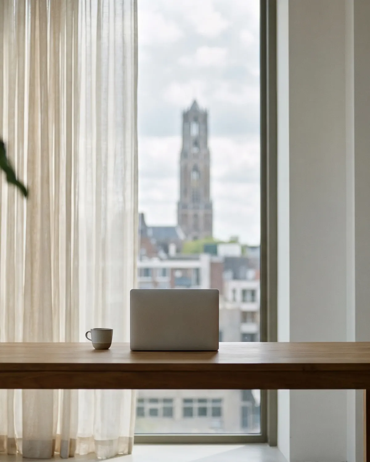 Een laptop op een lege tafel, met door het raam de Domtoren.