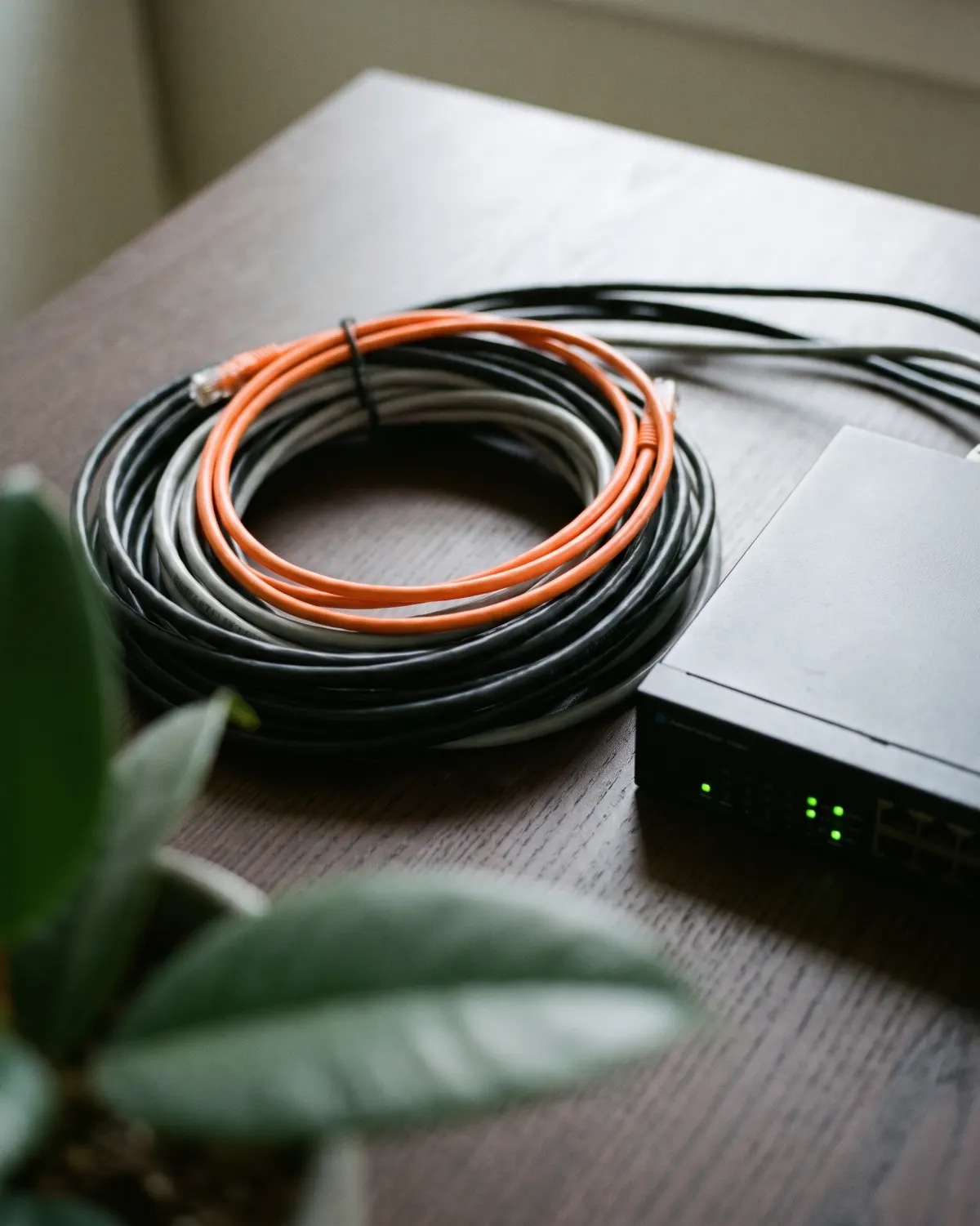 Een rol netwerkkabels naast een switch met groene lampjes op een houten tafel.